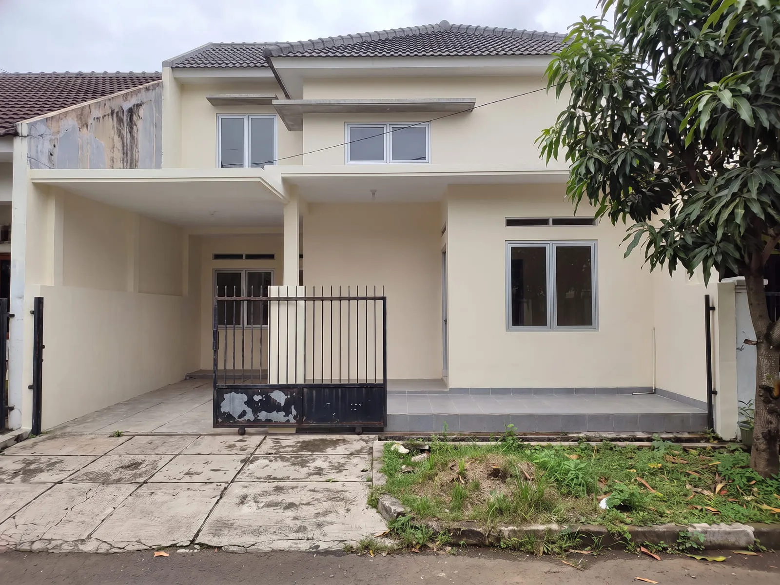 Rumah yang sama setelah dinaikkan menjadi dua lantai, dengan dinding plester dicat ulang, dua jendela di lantai atas beserta kanopi beton tipis, atap baru bergenteng abu-abu, dan teras berkeramik baru.