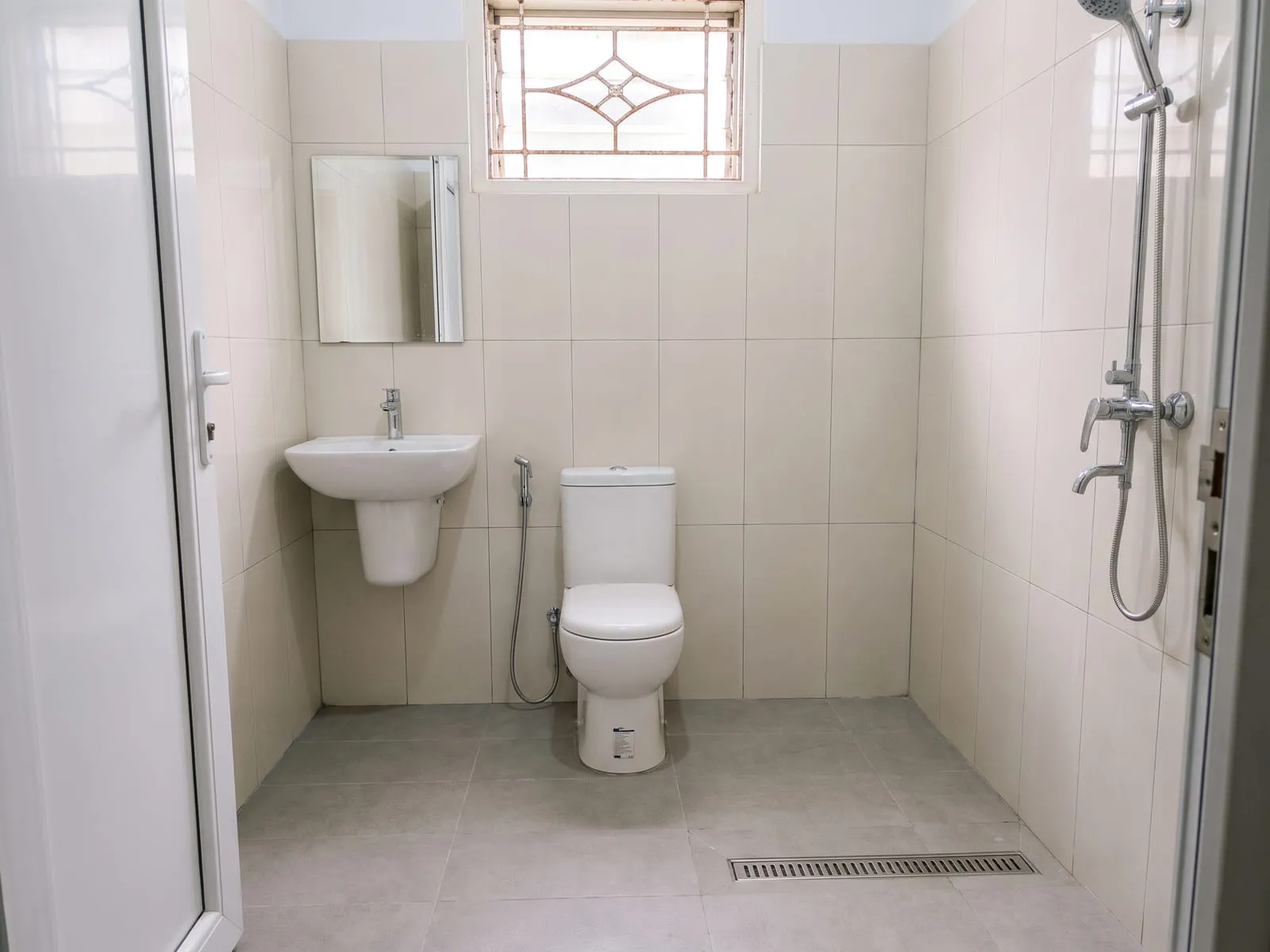 Kamar mandi yang sama setelah dikerjakan, dengan keramik lantai anti-licin, keramik dinding berukuran besar, kloset duduk, shower, dan wastafel gantung.
