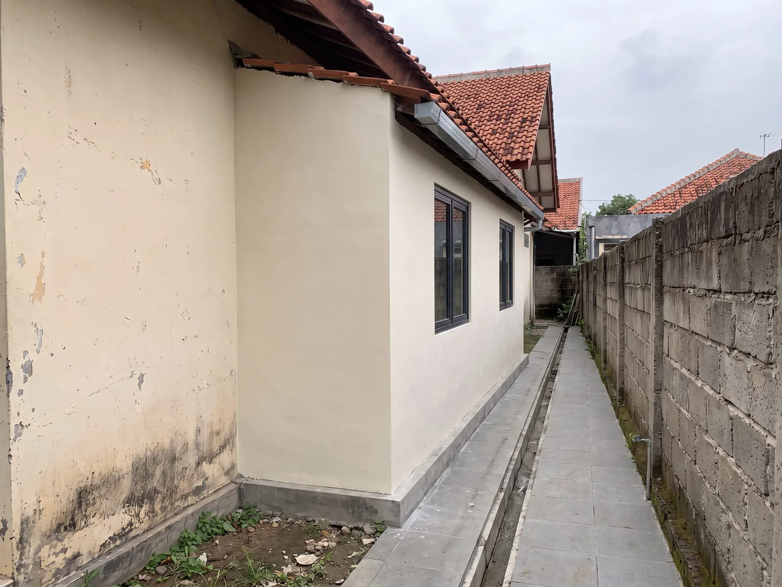 Sisi yang sama setelah dibangun kamar tambahan berdinding plester rapi dengan dua jendela dan atap yang disambungkan ke atap rumah lama.