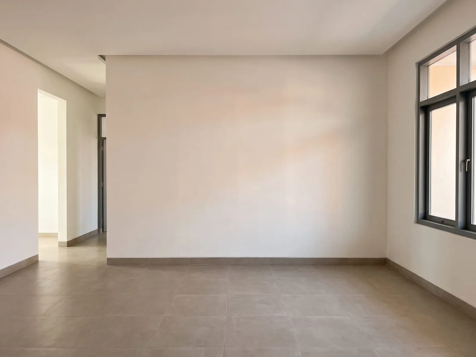 Ruang tamu yang sama setelah dikerjakan, berlantai keramik besar warna hangat, dinding dicat putih, plafon gipsum rata, dan jendela besar di dinding yang sama dengan kusen abu-abu tua.